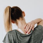 A woman in casual clothing holds her neck, indicating pain or discomfort.