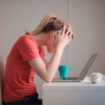 Young woman feeling stressed while studying at home with a laptop and coffee cup.