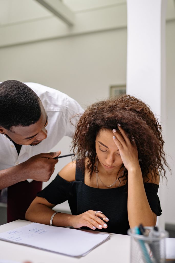 An adult man scolds a distressed woman in an office setting, illustrating workplace tension.