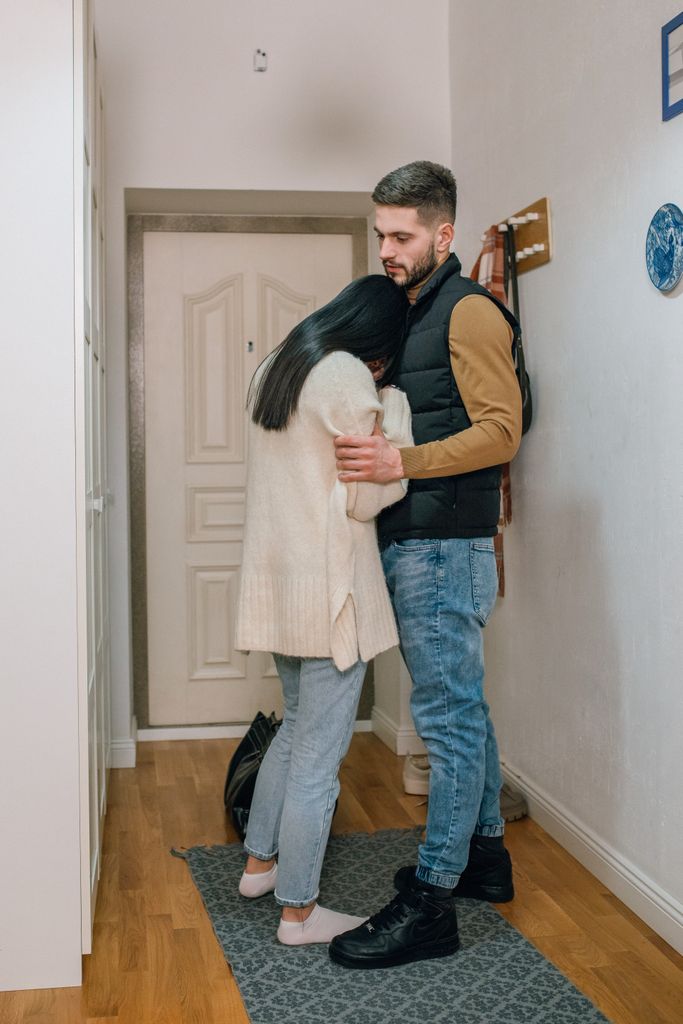 An emotional couple embraces in a hallway, conveying sadness and comfort at home.